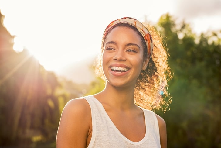 Portrait of beautiful african american woman smiling and looking away at park during sunset. Outdoor portrait of a smiling black girl. Happy cheerful girl laughing at park with colored hair band.