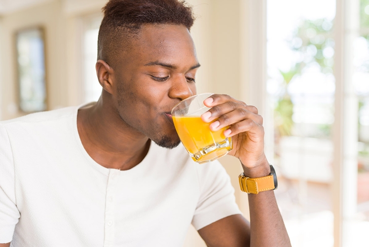 Handsome young african man drinking a glass of fresh natural orange juice enjoying fruit refreshment