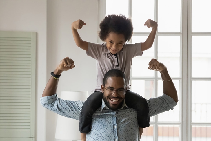 Small son sit on strong dad shoulders showing biceps. African family enjoy activity games at home, healthy fit lifestyle, two superheroes, vitamins for adults and children ad, happy Father Day concept