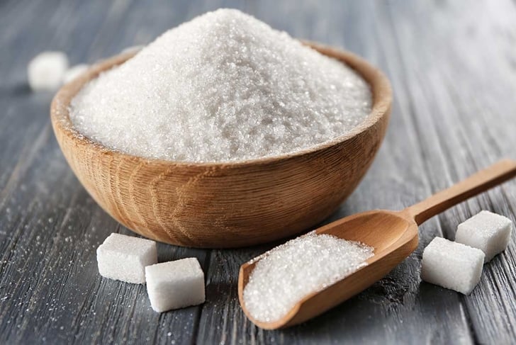 Bowl and scoop with white sand and lump sugar on wooden background