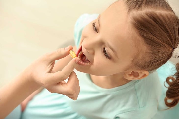 Young mother giving pill to her daughter, indoors