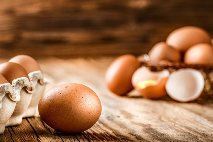 Brown eggs in carton box. Broken egg with yolk in background.